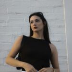 Elegant female model poses in front of a white brick wall during daytime, showcasing modern fashion.